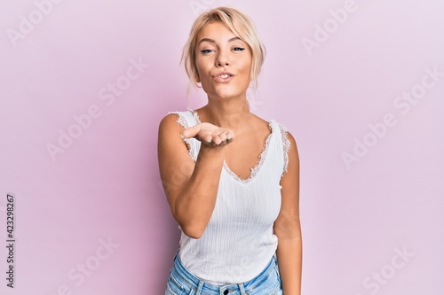 Young blonde girl wearing casual clothes looking at the camera blowing a kiss with hand on air being lovely and sexy. love expression.