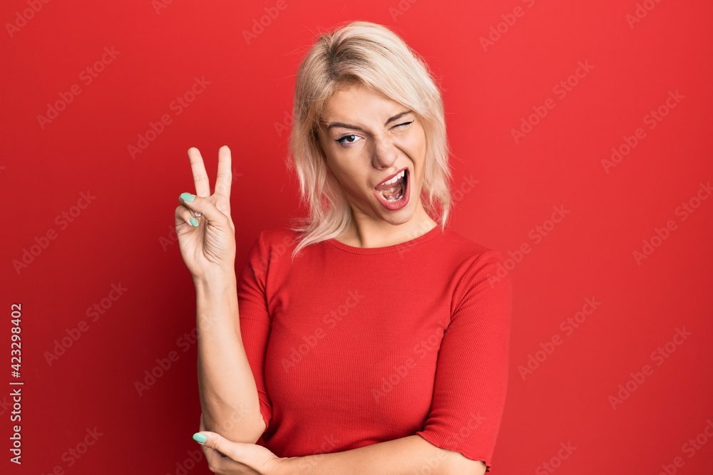 Young blonde girl wearing casual clothes smiling with happy face winking at the camera doing victory sign. number two. Young blonde girl wearing casual clothes smiling with happy face winking at the camera doing victory sign. number two.