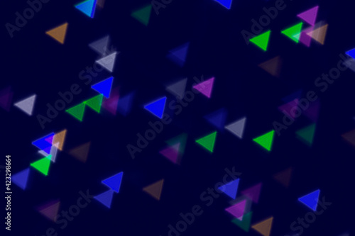 Defocused image of colored triangular shapes on an abstract background. Dark-blue background, blur bokeh.