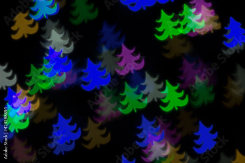 Defocused image of multi-colored Christmas trees on an abstract background. Dark background, blur bokeh.
