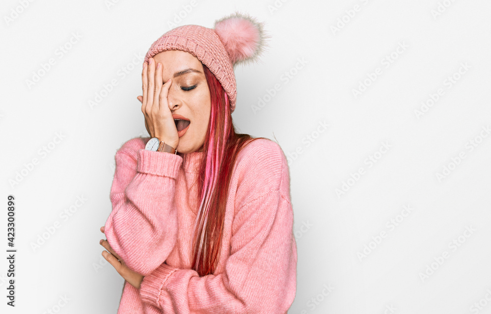 Young caucasian woman wearing casual clothes and wool cap yawning tired covering half face, eye and mouth with hand. face hurts in pain. Young caucasian woman wearing casual clothes and wool cap yawning tired covering half face, eye and mouth with hand. face hurts in pain.
