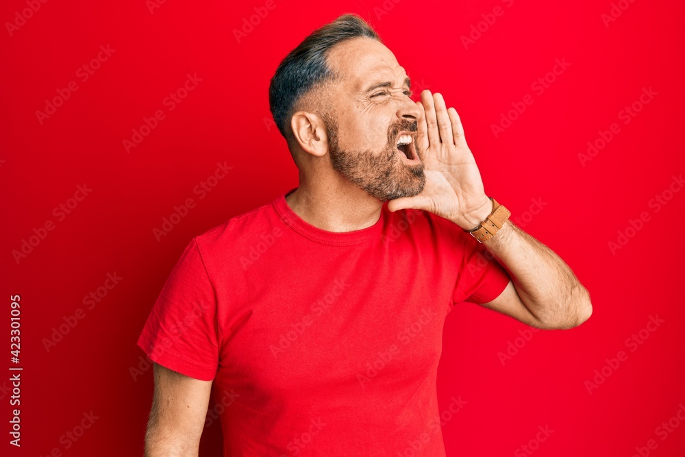 Handsome middle age man wearing casual red tshirt shouting and screaming loud to side with hand on mouth. communication concept. Handsome middle age man wearing casual red tshirt shouting and screaming loud to side with hand on mouth. communication concept.