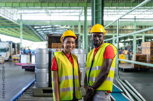 Portrait of Smiling African American worker looking camera in the Industry warehouse. Black female and male laborer in safety vest, hard hat working in a factory. Concept of Industrial manufacturing