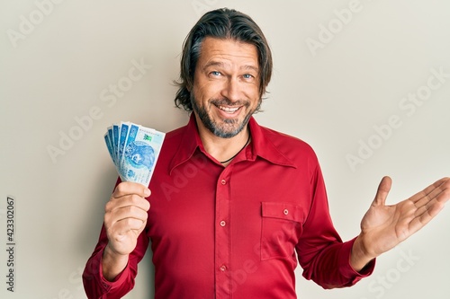 Middle age handsome man holding 50 polish zloty banknotes celebrating achievement with happy smile and winner expression with raised hand