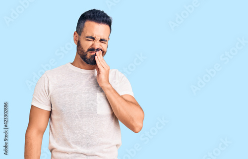 Young hispanic man wearing casual clothes touching mouth with hand with painful expression because of toothache or dental illness on teeth. dentist