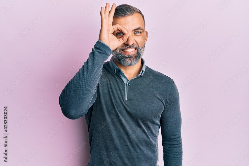 Middle age handsome man wearing casual clothes doing ok gesture with hand smiling, eye looking through fingers with happy face. Middle age handsome man wearing casual clothes doing ok gesture with hand smiling, eye looking through fingers with happy face.