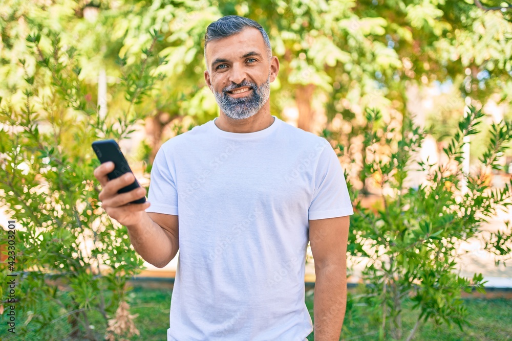 Middle age grey-haired man smiling happy using smartphone at the park Middle age grey-haired man smiling happy using smartphone at the park