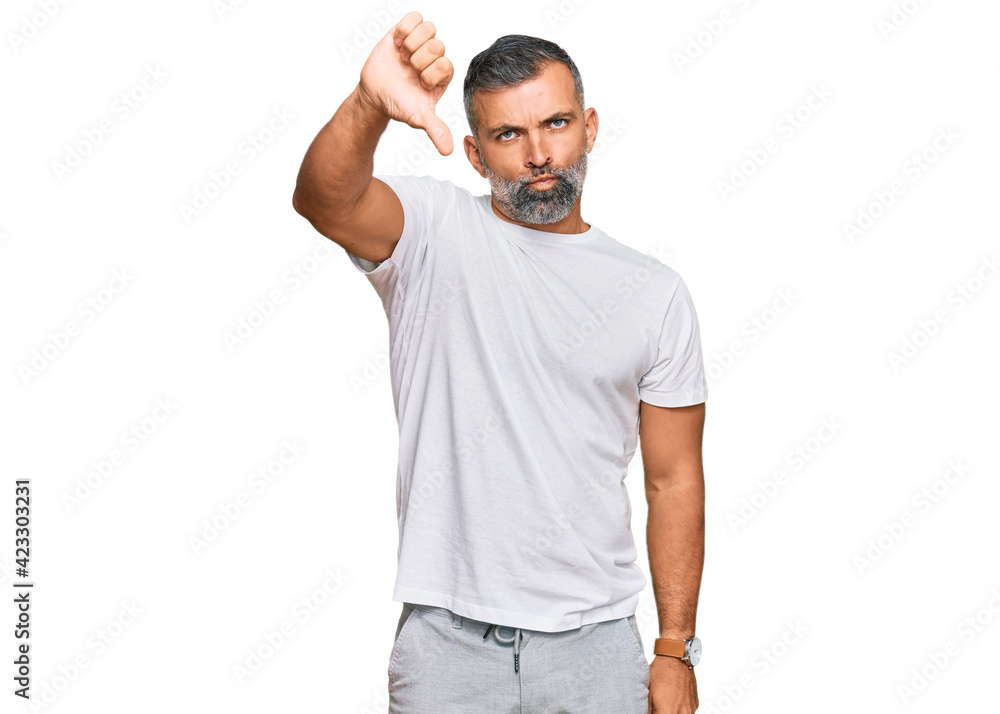 Middle age handsome man wearing casual white tshirt looking unhappy and angry showing rejection and negative with thumbs down gesture. bad expression. Middle age handsome man wearing casual white tshirt looking unhappy and angry showing rejection and negative with thumbs down gesture. bad expression.