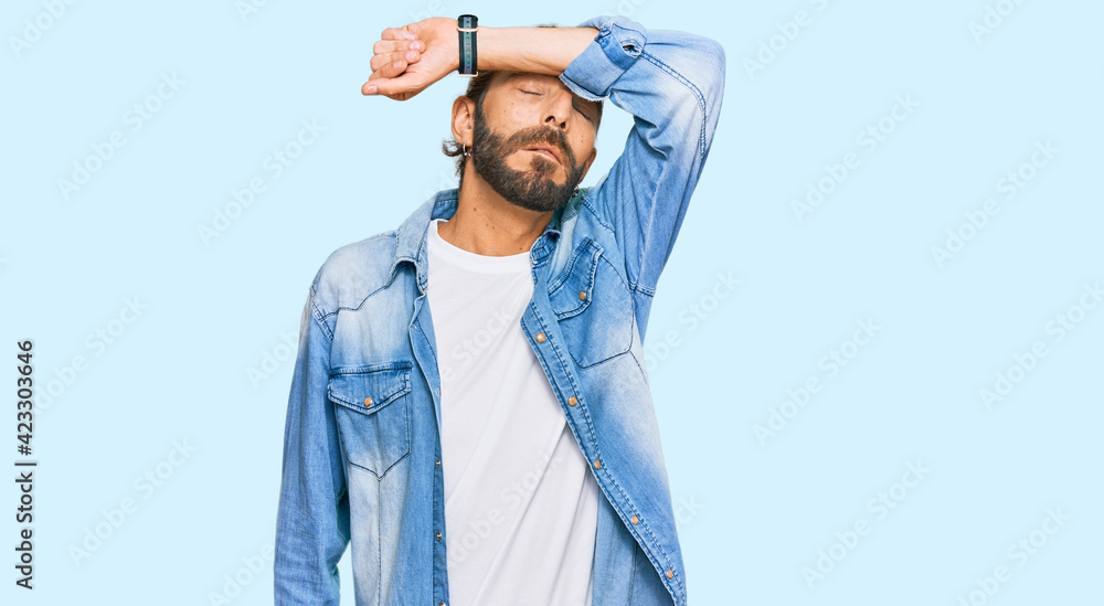 Attractive man with long hair and beard wearing casual denim jacket covering eyes with arm, looking serious and sad. sightless, hiding and rejection concept Attractive man with long hair and beard wearing casual denim jacket covering eyes with arm, looking serious and sad. sightless, hiding and rejection concept