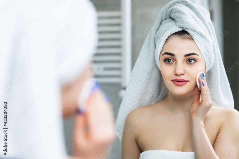 Portrait of beautiful woman in bathrobe and with towel on her head cleaning her face with sponge and smiling in bathroom Portrait of beautiful woman in bathrobe and with towel on her head cleaning her face with sponge and smiling in bathroom