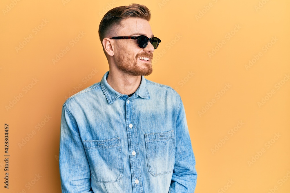 Fototapeta premium Young redhead man wearing stylish sunglasses looking away to side with smile on face, natural expression. laughing confident.