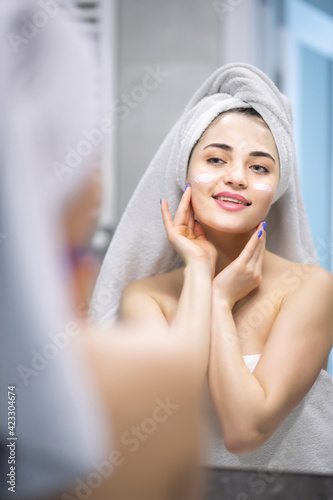 Attractive girl putting anti-aging cream on her face after shower in bathroom