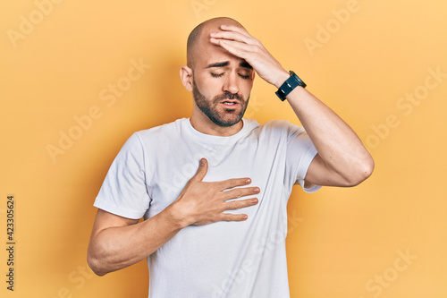 Young bald man wearing casual white t shirt touching forehead for illness and fever, flu and cold, virus sick