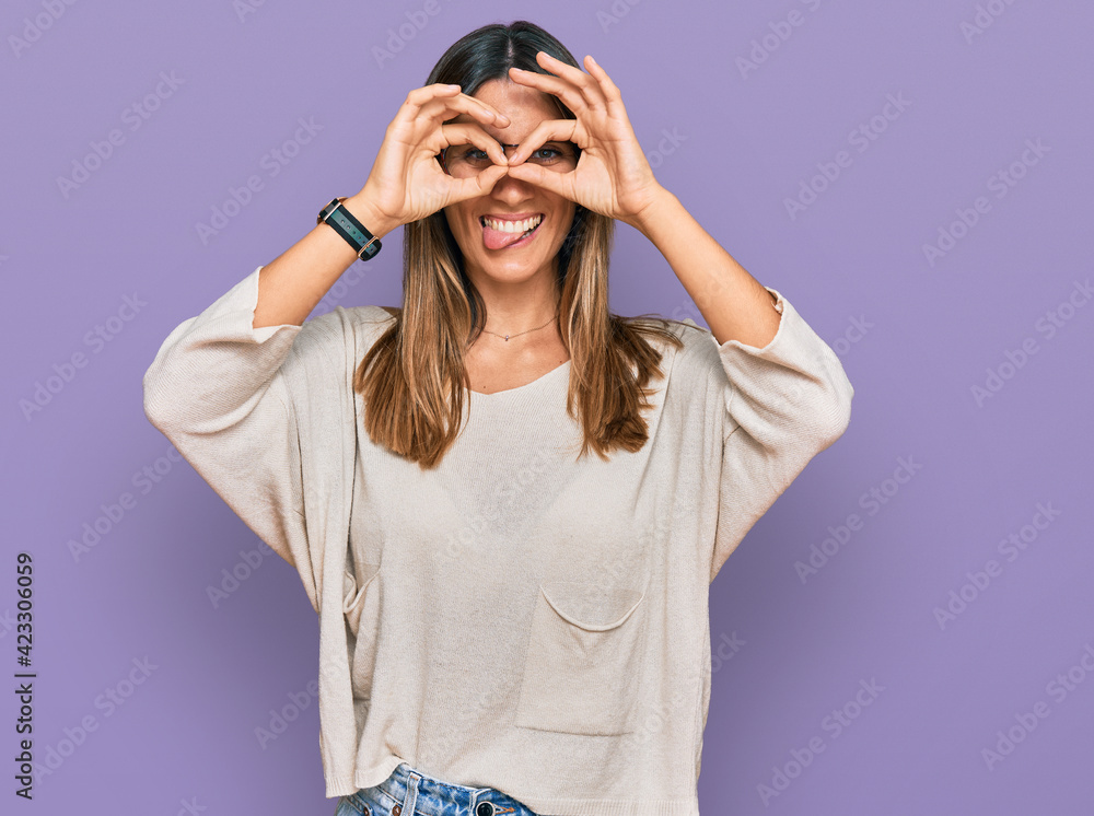 Young woman wearing casual clothes and glasses doing ok gesture like binoculars sticking tongue out, eyes looking through fingers. crazy expression. Young woman wearing casual clothes and glasses doing ok gesture like binoculars sticking tongue out, eyes looking through fingers. crazy expression.
