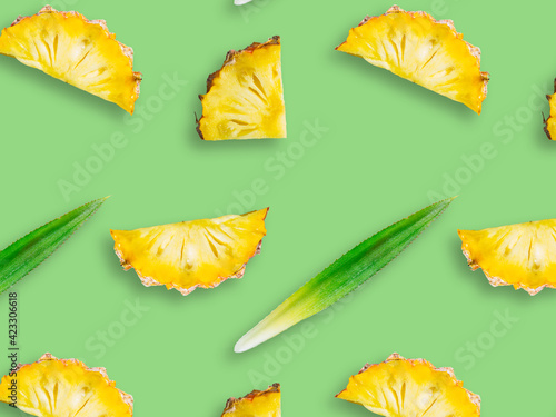 Seamless pattern of fresh ripe pineapple slices and leaves isolated on green background. Top view. Exotic tropical fruit summer concept