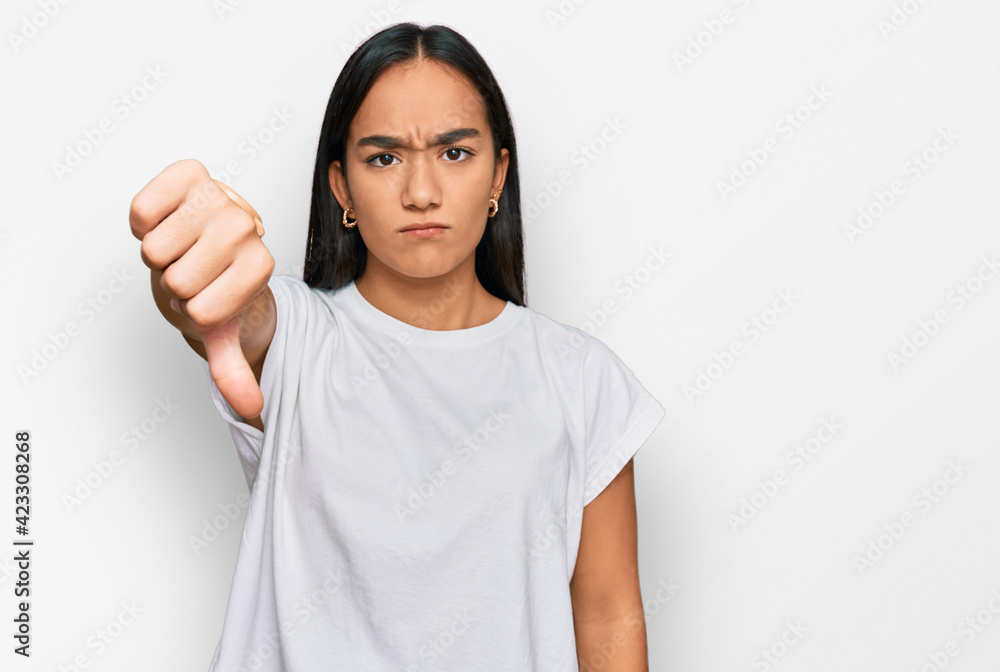 Young asian woman wearing casual white t shirt looking unhappy and angry showing rejection and negative with thumbs down gesture. bad expression. Young asian woman wearing casual white t shirt looking unhappy and angry showing rejection and negative with thumbs down gesture. bad expression.