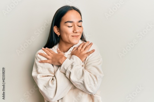 Young asian woman wearing casual sweatshirt hugging oneself happy and positive, smiling confident. self love and self care