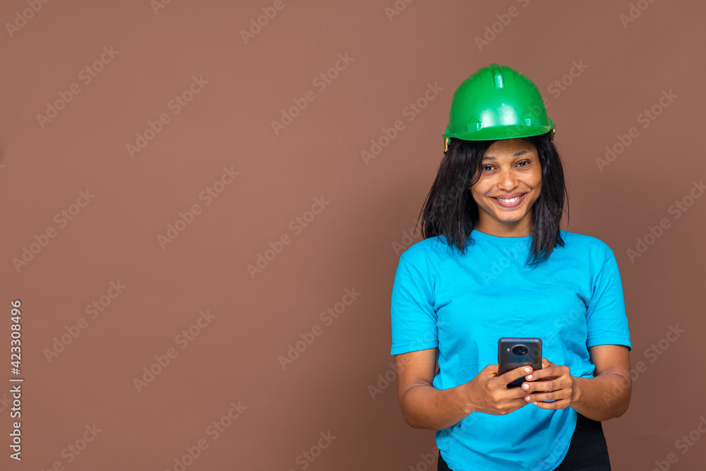 portrait of an attractive young black female contractor wearing a hard hat, using her phone
