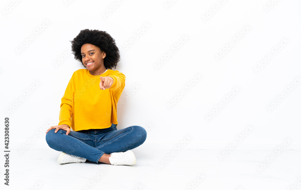 Young African American woman sitting on the floor points finger at you with a confident expression Young African American woman sitting on the floor points finger at you with a confident expression