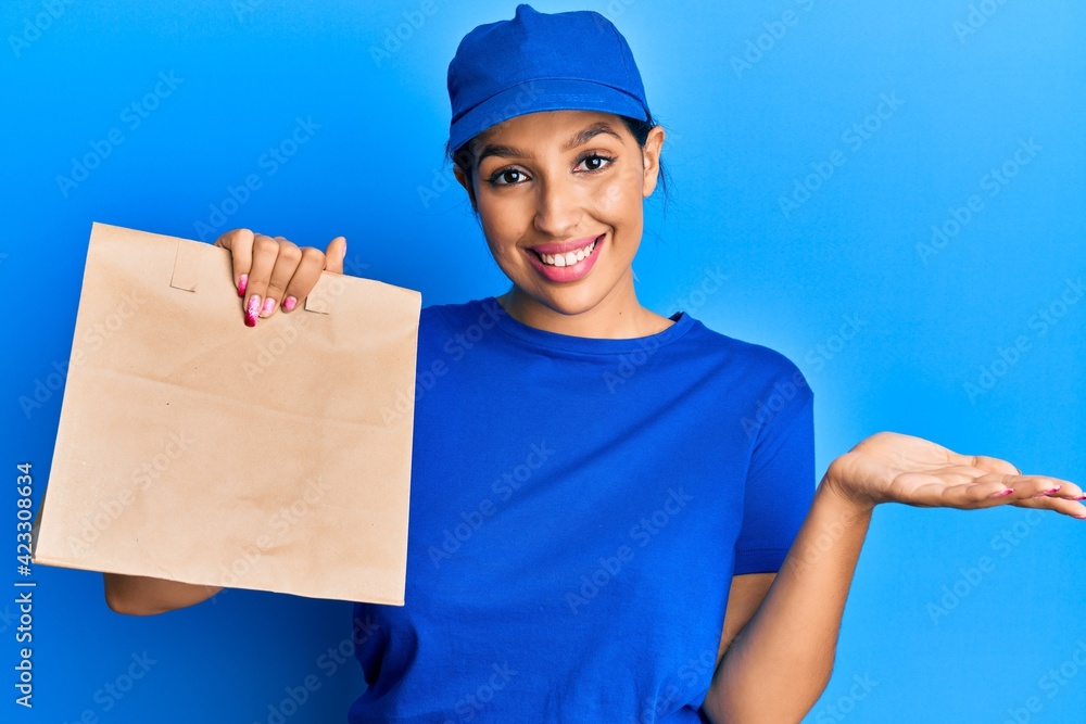 Beautiful brunette woman holding take away paper bag celebrating achievement with happy smile and winner expression with raised hand Beautiful brunette woman holding take away paper bag celebrating achievement with happy smile and winner expression with raised hand