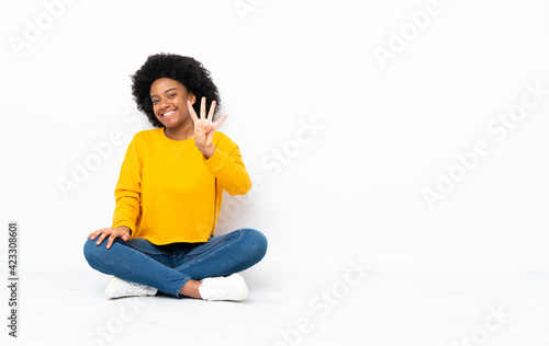 Young African American woman sitting on the floor happy and counting four with fingers © luismolinero