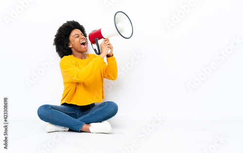 Young African American woman sitting on the floor shouting through a megaphone
