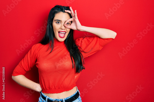 Young hispanic girl wearing casual clothes smiling happy doing ok sign with hand on eye looking through fingers