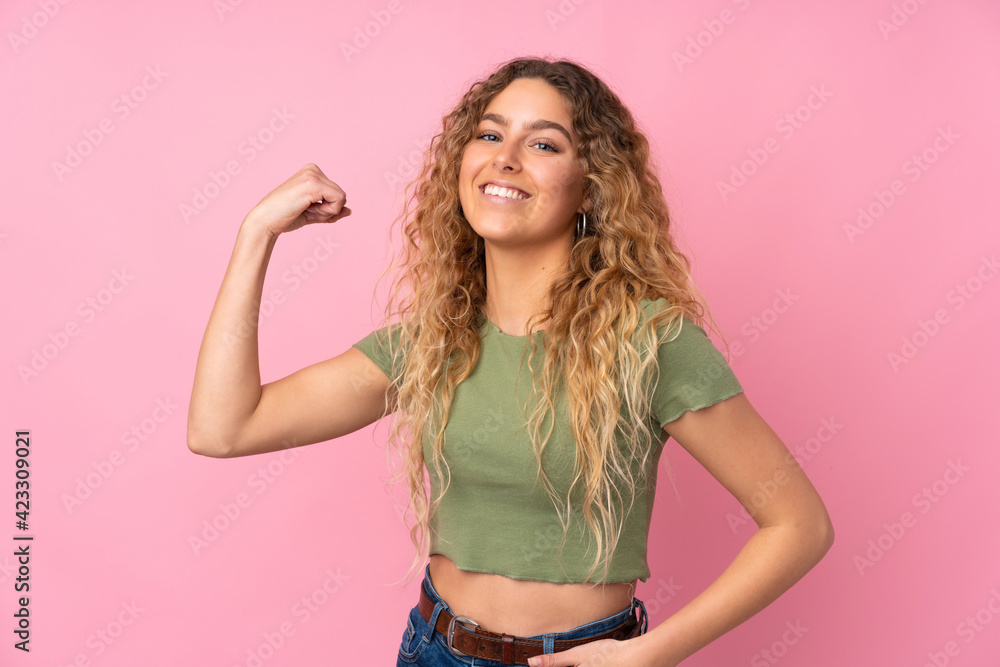 Young blonde woman with curly hair isolated on pink background doing strong gesture Young blonde woman with curly hair isolated on pink background doing strong gesture