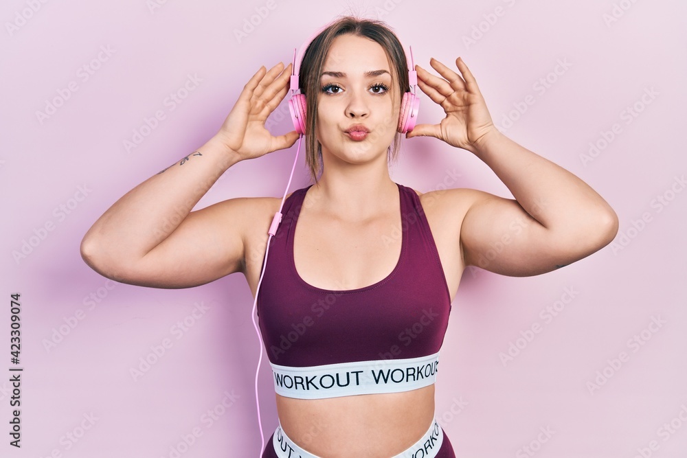 Young hispanic girl wearing gym clothes and using headphones looking at the camera blowing a kiss being lovely and sexy. love expression.