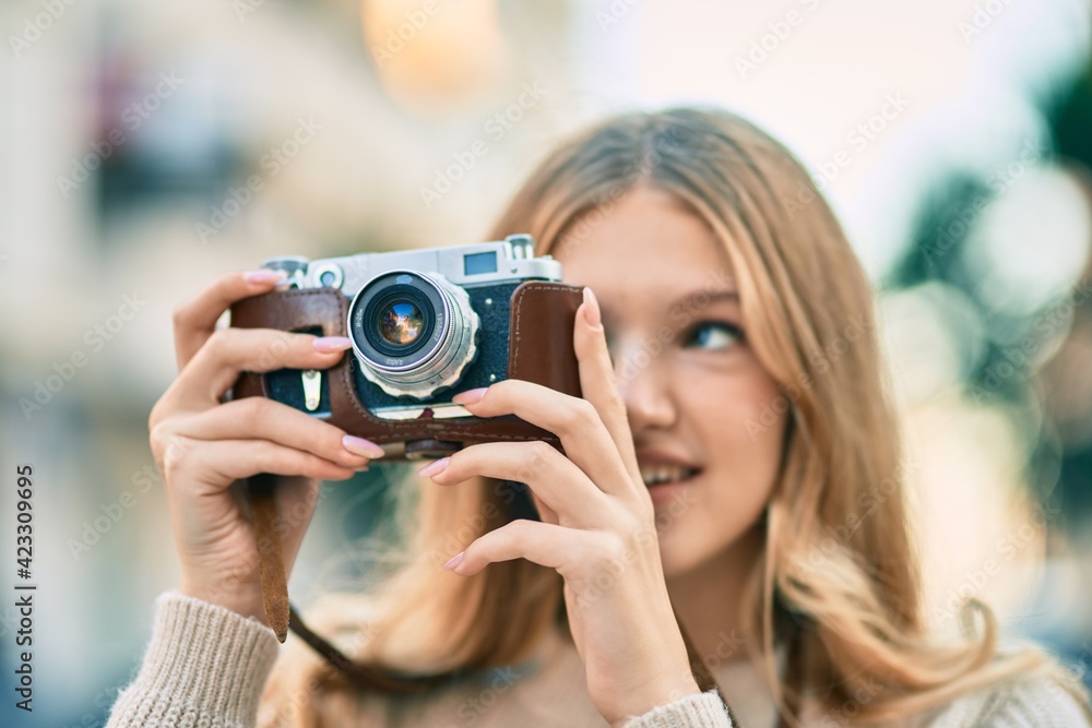 Beautiful caucasian teenager smiling happy using vintage camera at the city.