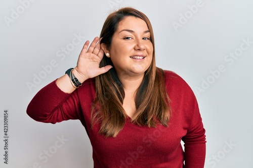 Beautiful brunette plus size woman wearing casual clothes smiling with hand over ear listening and hearing to rumor or gossip. deafness concept.