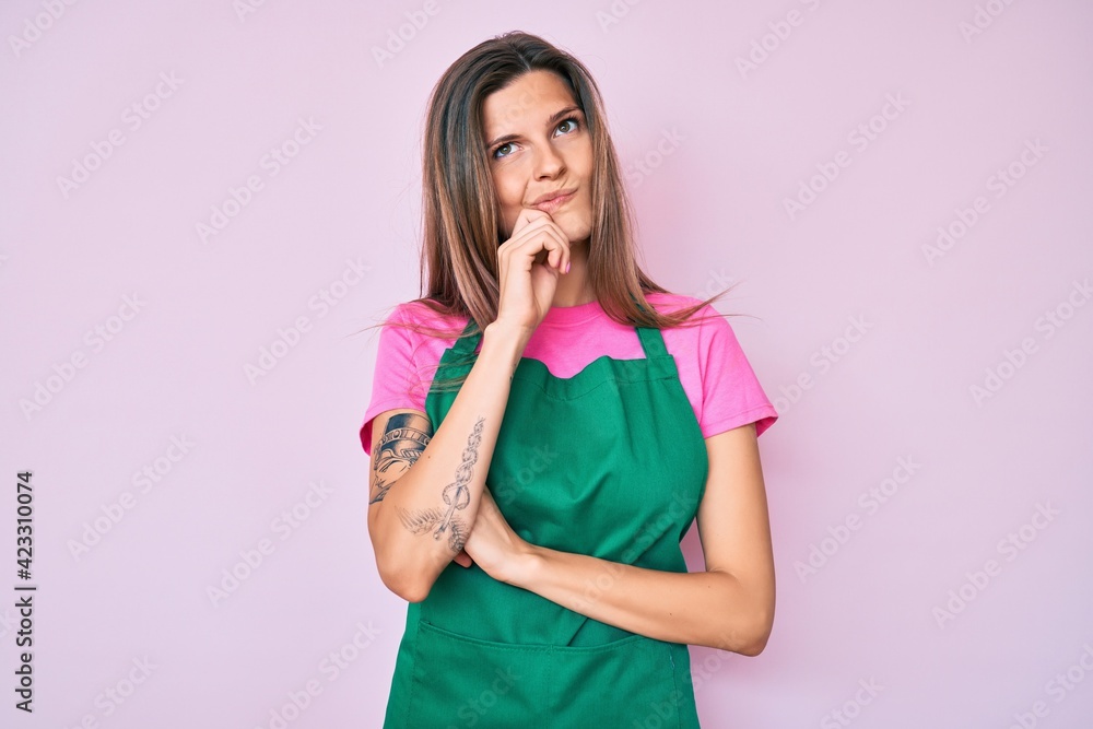 Beautiful caucasian woman wearing professional apron serious face thinking about question with hand on chin, thoughtful about confusing idea Beautiful caucasian woman wearing professional apron serious face thinking about question with hand on chin, thoughtful about confusing idea