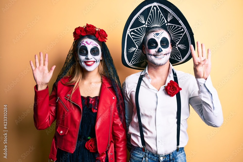 Couple wearing day of the dead costume over yellow showing and pointing up with fingers number nine while smiling confident and happy.
