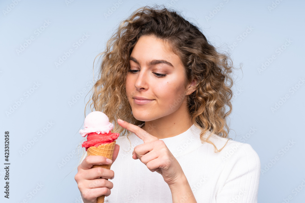 Young blonde woman with curly hair holding a cornet ice cream isolated on blue background