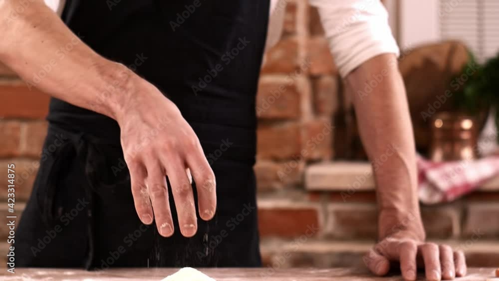 Close-up of man in black apron pours flour in kitchen. Baker sprinkles pinch of flour on baking Close-up of man in black apron pours flour in kitchen. Baker sprinkles pinch of flour on baking