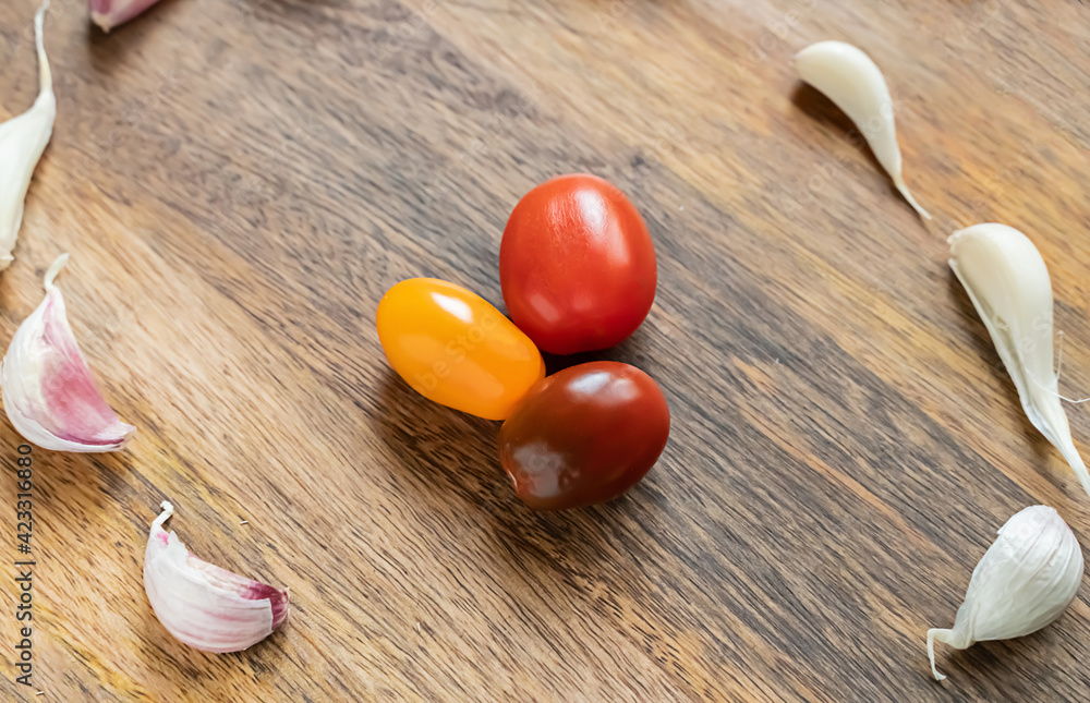yellow and red tomatoes in the center of scattered cloves of garlic on wooden background yellow and red tomatoes in the center of scattered cloves of garlic on wooden background
