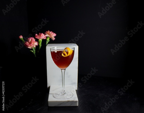 Red Deshler cocktail against white marble and a black background with pink flowers photo