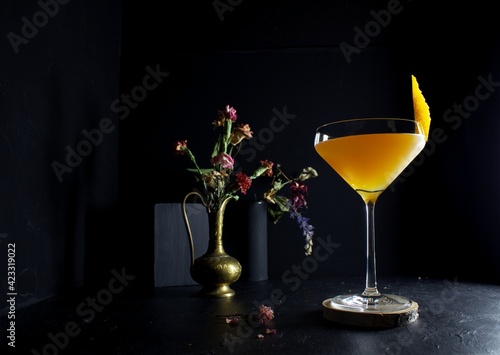 Yellow cocktail, coupe glass, orange garnish against a dark moody black background