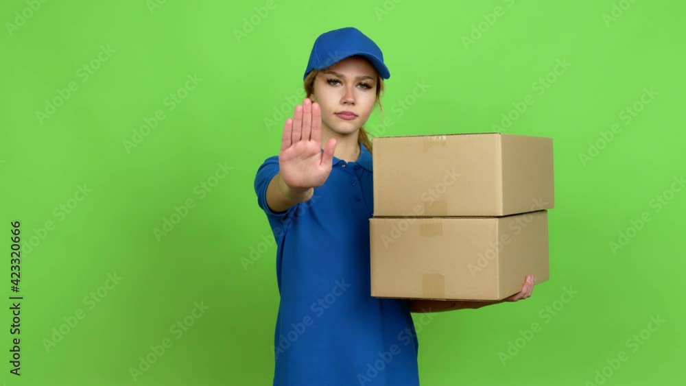 Young blonde teenager girl holding boxes for delivery doing stop sign over isolated background. Green screen chroma key Young blonde teenager girl holding boxes for delivery doing stop sign over isolated background. Green screen chroma key