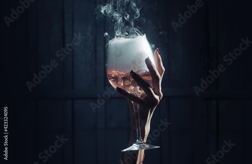 Closeup female hand holding wine glass of mysterious white crystalline material of liquid with foam on wooden dark background.