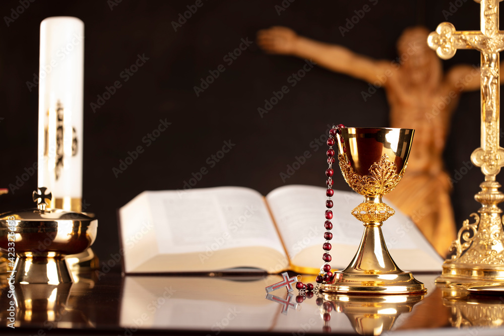 Fototapeta premium Religious holiday – Easter. Catholic symbols composition. Jesus figure, The Cross, monstrance, Holy Bible, rosary and golden chalice on gray background. 