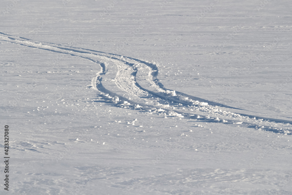 Long winding trails from a motorcycle snowmobile on the surface of a frozen river.