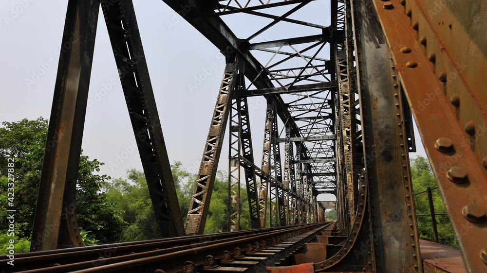 Metal pillar and old railway bridge structure. Details of a truss bridge type steel bridge connecting the bolts and bolts against the background of the afternoon blue sky. Selective focus Metal pillar and old railway bridge structure. Details of a truss bridge type steel bridge connecting the bolts and bolts against the background of the afternoon blue sky. Selective focus