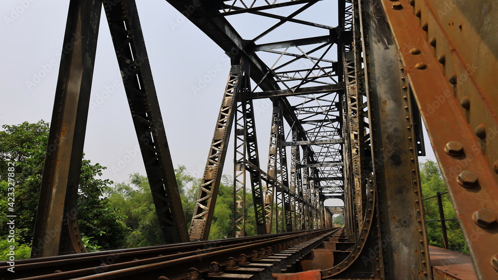 Metal pillar and old railway bridge structure. Details of a truss bridge type steel bridge connecting the bolts and bolts against the background of the afternoon blue sky. Selective focus