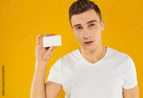 A guy in a white t-shirt shows a credit card on a yellow background cropped view