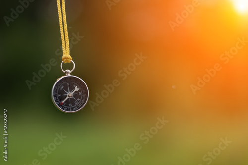 small tourist compass like a pendulum on a green blurred nature background. Search and hiking concept.