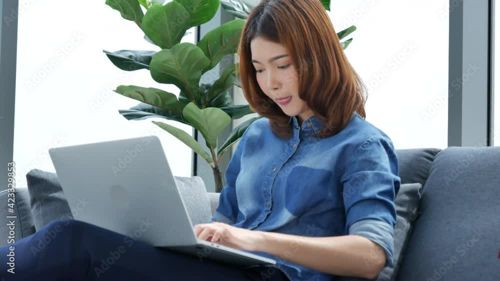 Woman working from home on laptop online meeting in home office. Entrepreneur asian business woman using notebook laptop sit on sofa technology new normal lifestyle. Happy woman typing keyboard laptop Woman working from home on laptop online meeting in home office. Entrepreneur asian business woman using notebook laptop sit on sofa technology new normal lifestyle. Happy woman typing keyboard laptop