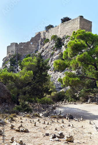 Greece. Rhodes Island. The stone walls of a medieval knight's fortified castle Monolithos (1476) and the tourist stone pyramids on the uphill path. Famous tourist attraction of the island photo