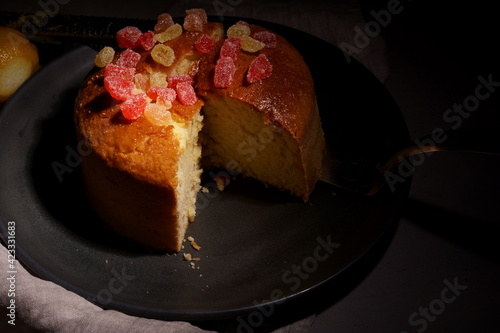 Sliced lemon sponge cake with candied fruits on a dark background. Fluffy sponge cake with marmalade on a dark plate.