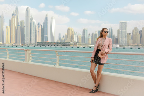 Beautiful girl standing on embankment against the backdrop of metropolis with skyscrapers. Urban style. Copy space. Dubai, UAE. 